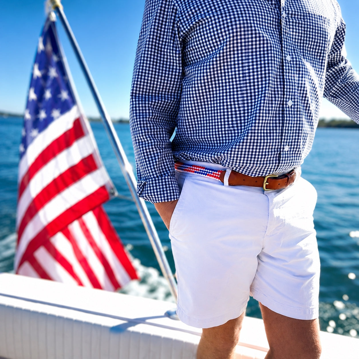 Person on a boat wearing a checkered shirt and white shorts with an American flag in the background.